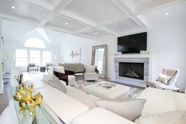 Bright modern living room with white sectional sofa, fireplace, wall-mounted TV, and large windows for natural light