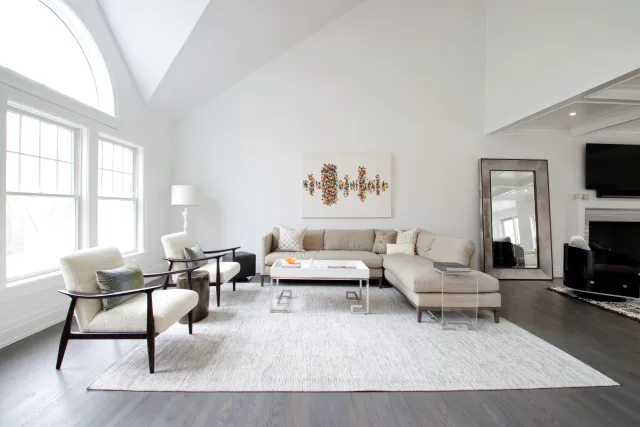 Bright modern living room with large arched window, beige sectional sofa, armchairs, and abstract wall art