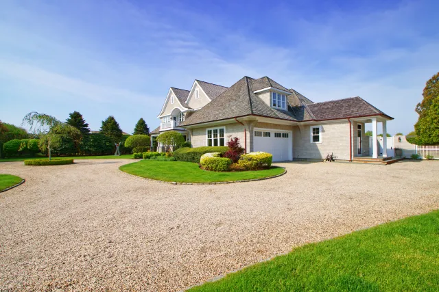 Large suburban home with a gravel driveway, manicured lawn, and clear blue sky on a sunny day.