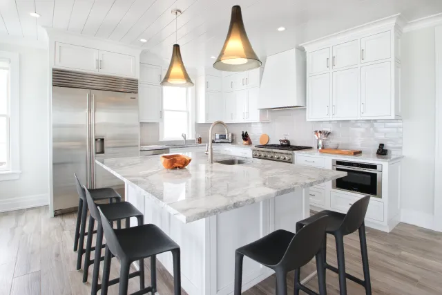 Bright modern kitchen with marble island, black bar stools, stainless steel appliances, and white cabinetry