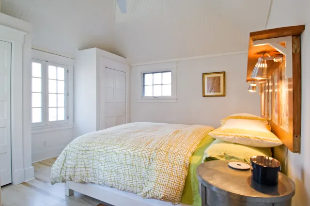 Bright bedroom with vaulted ceiling featuring a white and yellow patterned bedspread and wooden headboard.