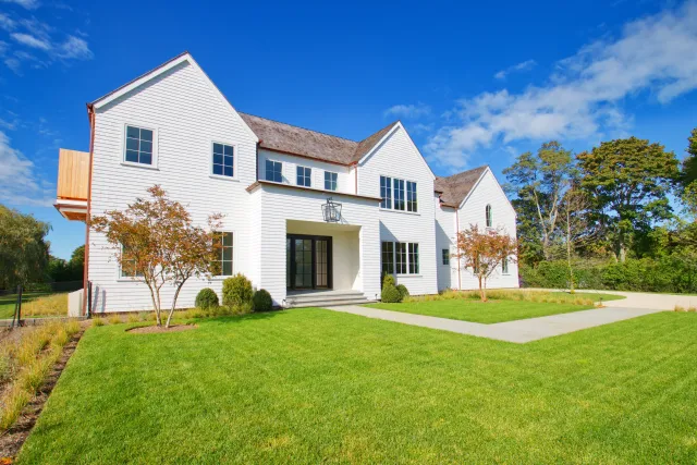 Modern two-story white house with large windows, green lawn, and clear blue sky on a sunny day