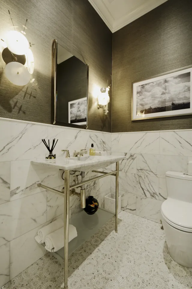 Modern bathroom with marble sink, metal frame, patterned tile floor, wall sconces, and framed artwork.