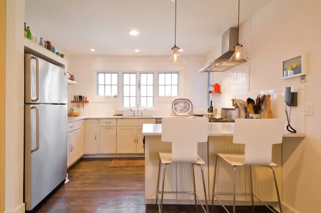 Bright modern kitchen with white cabinets, stainless steel refrigerator, island with stools, and wooden flooring