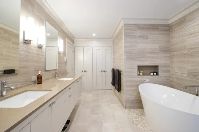 Modern bathroom with double sink vanity, large mirror, freestanding tub, and beige tiled walls and floors.