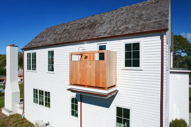 White house with a wooden outdoor shower balcony under clear blue sky and multiple windows