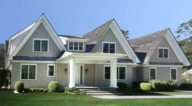 Spacious modern two-story house with steep gable roofs, large windows, front porch, and manicured lawn.