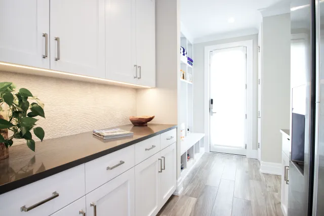 Bright modern kitchen with white cabinets, black countertop, wood flooring, and a backlit textured backsplash.