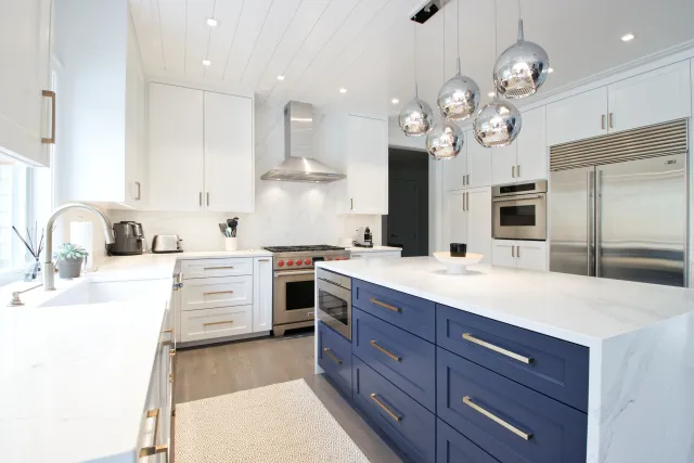 Modern kitchen with white cabinets, blue island, stainless steel appliances, and hanging globe pendant lights