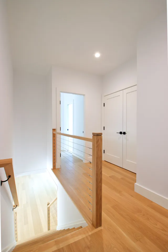 Modern bright hallway with wooden floors, white walls, metal cable railing, and double white doors.