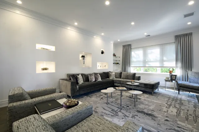 Modern living room with gray sectional sofa, patterned armchairs, decorative shelves, and large window with curtains.