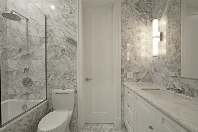 Modern bathroom with marble walls, bathtub with shower, white toilet, and marble countertop vanity with sink.
