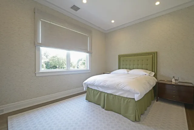 Bright bedroom with green upholstered bed, white bedding, wooden nightstands, and large window with roller shade.