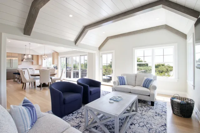 Bright living room with vaulted ceiling, blue armchairs, white sofa, wooden coffee table, and adjacent dining area.