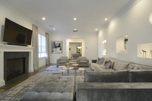 Modern living room with grey velvet sectional sofa, armchairs, fireplace, and wall-mounted TV under recessed lighting.