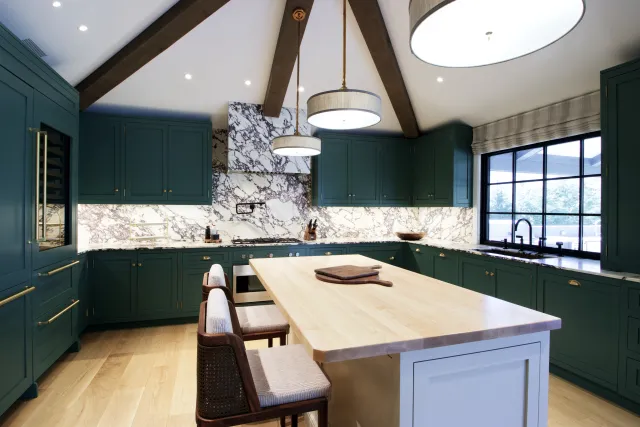 Modern kitchen with teal cabinets, marble backsplash, wooden island, and pendant lighting under vaulted ceiling