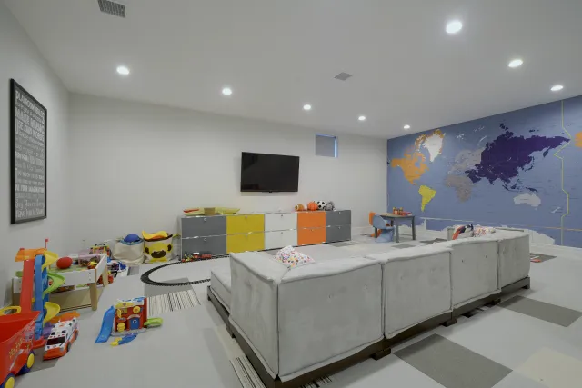 Modern playroom with gray sectional sofa, colorful storage units, toys, and a large world map mural on the wall.