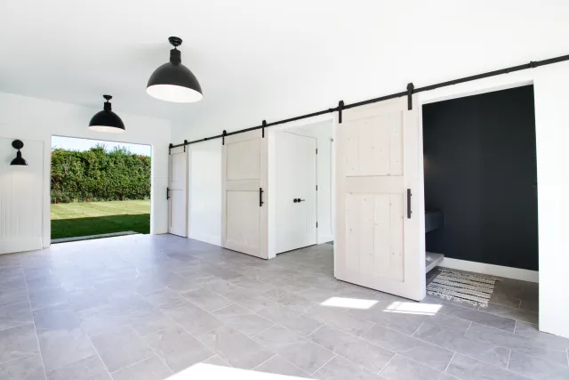 Bright modern room with sliding barn doors, gray tile floor, black light fixtures, and open view to green lawn outside