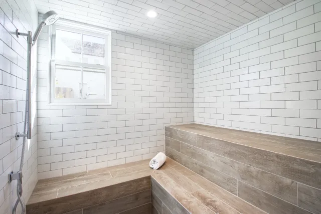 Modern steam shower with white subway tiles and wood-look benches under natural light
