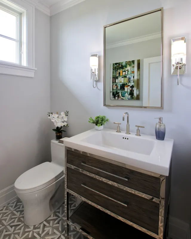 Modern bathroom with white toilet, wooden vanity, large mirror, and geometric floor tiles under natural light.