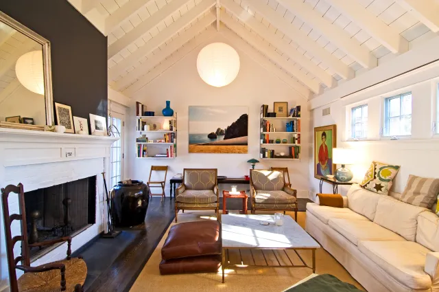 Bright living room with white vaulted ceiling, fireplace, beige sofa, wooden chairs, and coastal wall art.