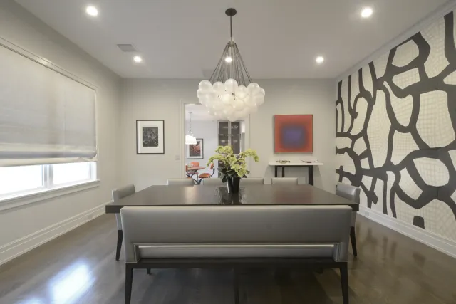 Modern dining room with a dark wood table, gray chairs, geometric black and white accent wall, and a bubble chandelier.