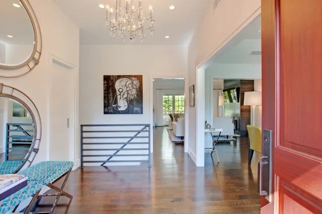 Bright home entryway with wooden floor, modern chandelier, round mirrors, and artwork on white walls.