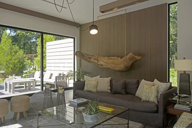 Modern living room with brown sofa, decorative driftwood, glass coffee table, and large sliding glass door to patio.