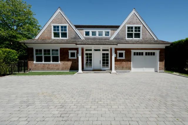 Modern two-story house with wooden shingles, white accents, large driveway, and attached garage under clear blue sky.