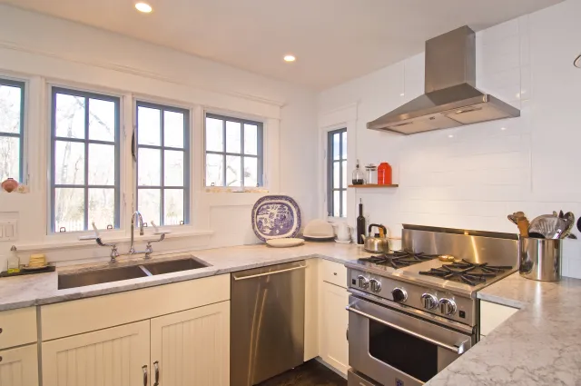Bright modern kitchen with stainless steel appliances, white cabinets, marble countertops, and large windows