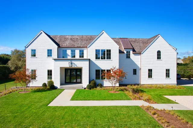 Modern white two-story house with large windows and manicured green lawn under a clear blue sky
