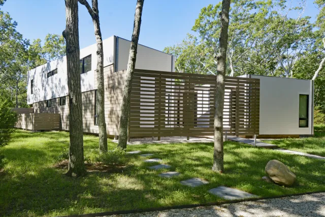 Modern white and beige minimalist house with wooden slat fence surrounded by trees and greenery on a sunny day
