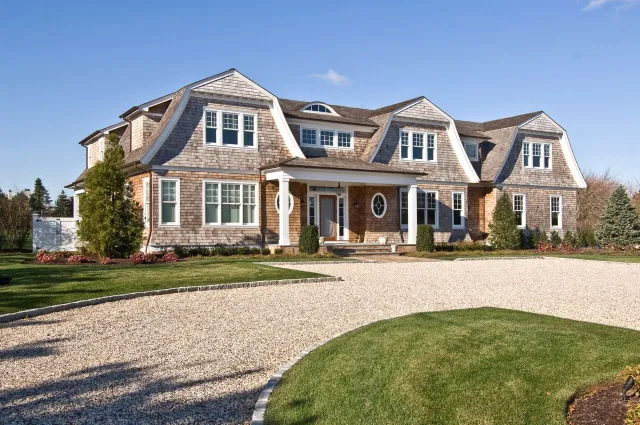 Stunning home exterior with manicured lawn, gravel driveway, and classic architectural design under a blue sky.