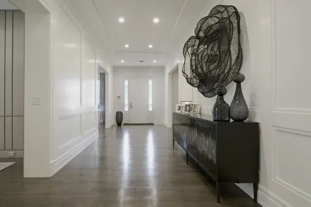 Modern hallway with white walls, hardwood floor, black console table, and artistic metal wall decor
