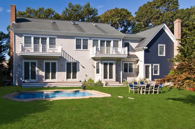 Modern two-story house with white and blue siding, backyard pool, patio furniture, and green lawn under clear sky