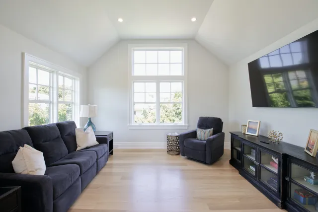 Bright living room with navy blue sofa and armchair, hardwood floor, large windows, and wall-mounted TV.