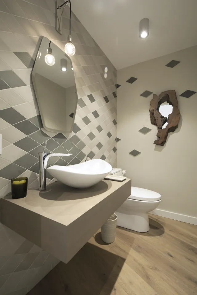 Modern bathroom with floating wooden vanity, unique vessel sink, geometric wall tiles, and sculptural mirror.