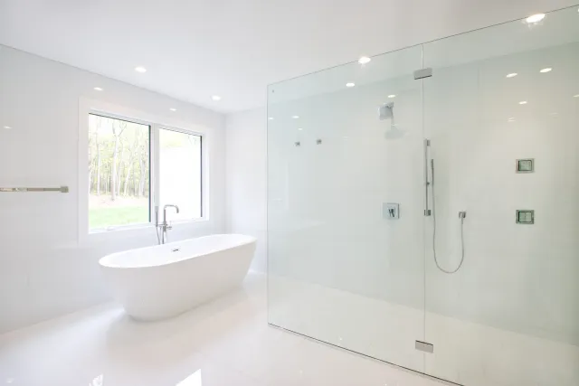 Bright modern bathroom with freestanding tub, large glass shower, white tiles, and natural light from window.