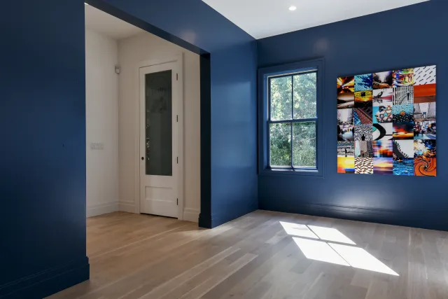 Empty room with dark blue walls, light wood flooring, a white door, window, and colorful abstract artwork.