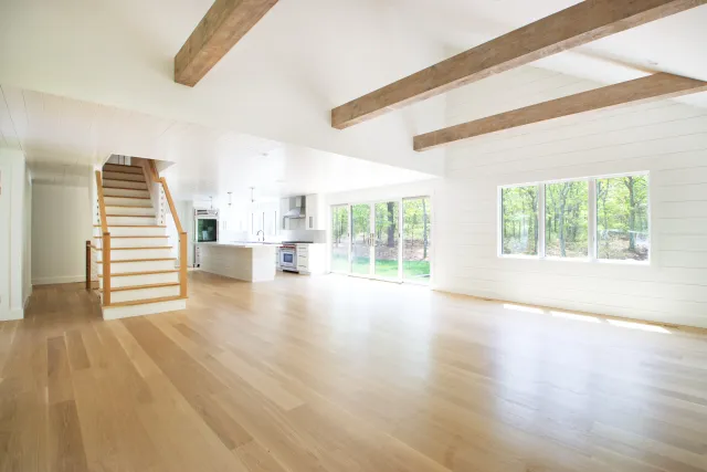 Bright open floor plan home with wooden floors, exposed beams, large windows, and modern kitchen.