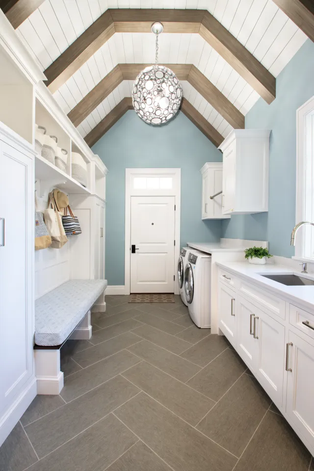 Bright laundry room with vaulted ceiling, white cabinetry, bench seating, washer and dryer, and a modern pendant light.