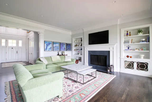 Bright living room with light green sofas, marble coffee table, fireplace, built-in shelves, and patterned rug on hardwood floor