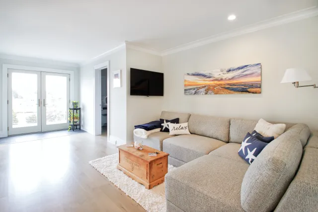 Bright living room with gray sectional sofa, wooden coffee table, wall-mounted TV, and large glass doors