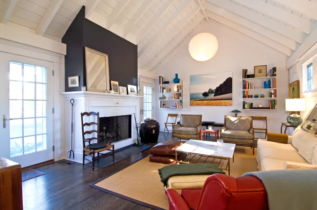 Bright living room with white vaulted ceiling, dark wood floor, fireplace, sofas, armchairs, and large wall art.
