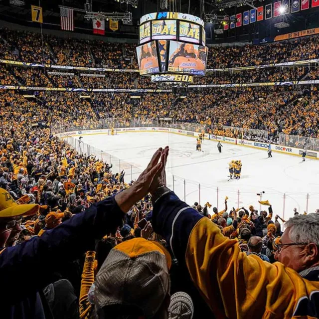 Fans in yellow cheering and high-fiving during a live hockey game in a packed arena with scoreboard showing a goal
