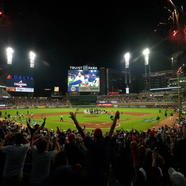 Excited crowd at Truist Park celebrating a baseball championship victory under stadium lights at night