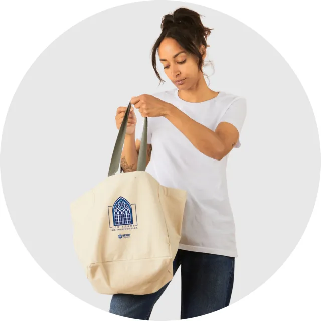 Woman in white t-shirt holding beige tote bag with blue stained glass window design and text.