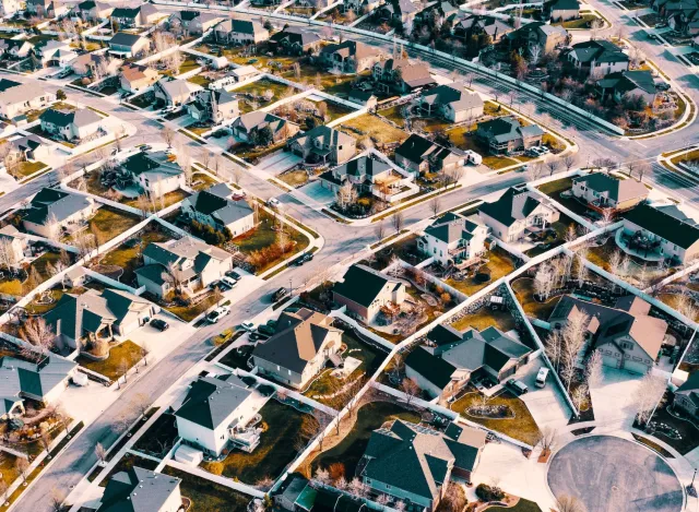 Aerial view of a suburban neighborhood with houses, curved roads, and landscaped yards in daytime.