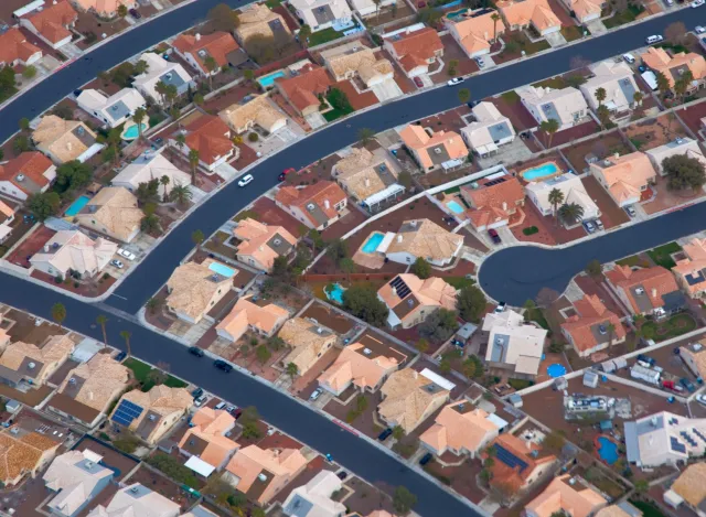 Aerial view of a suburban neighborhood with houses, winding roads, and some with swimming pools and solar panels.