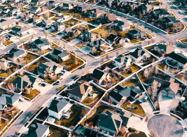 Aerial view of a suburban neighborhood with winding roads, houses, and green lawns under sunlight.